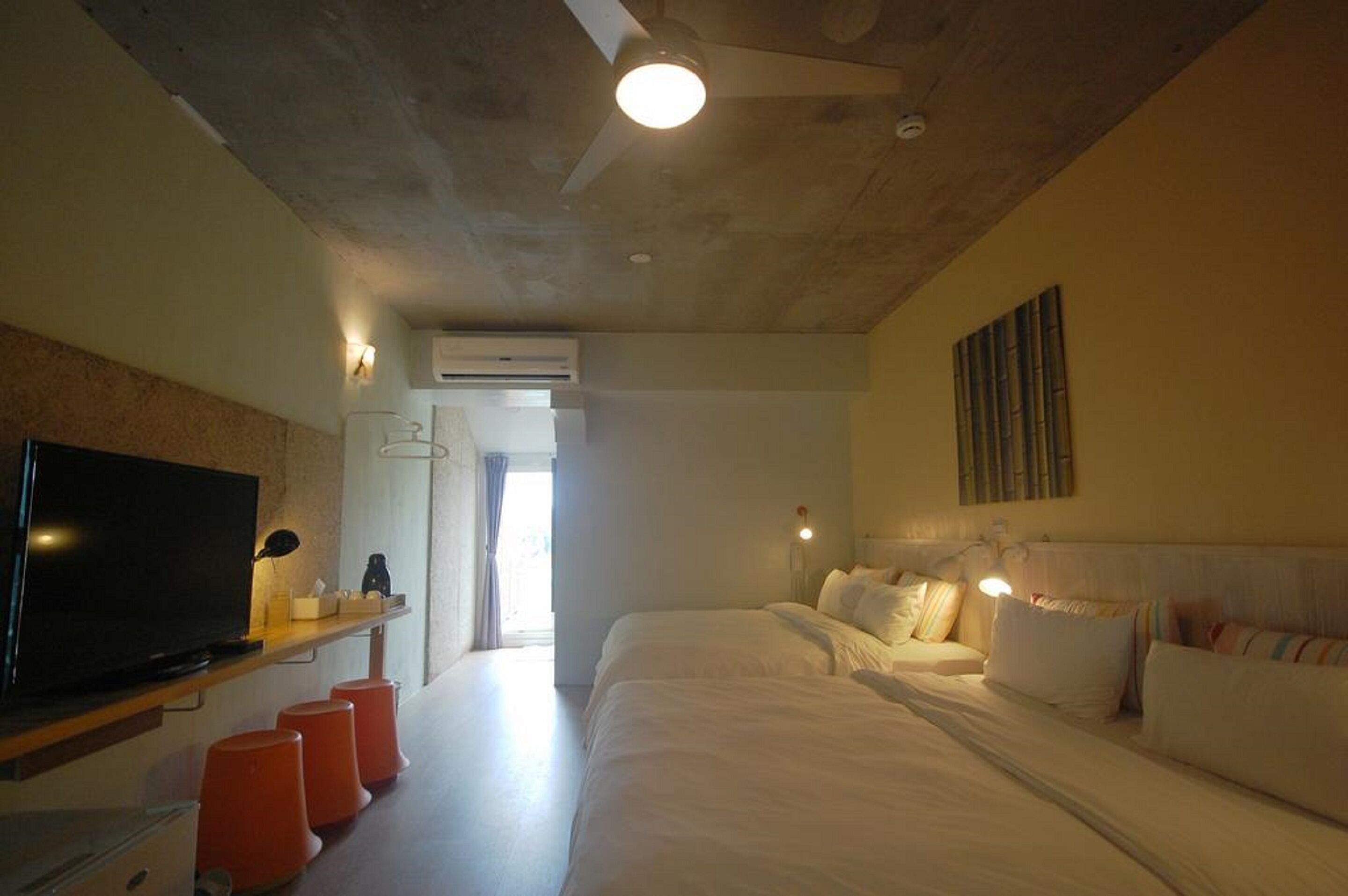 Habitación de hotel con televisor de pantalla plana, dos camas, ventilador de techo y un ventanal grande.