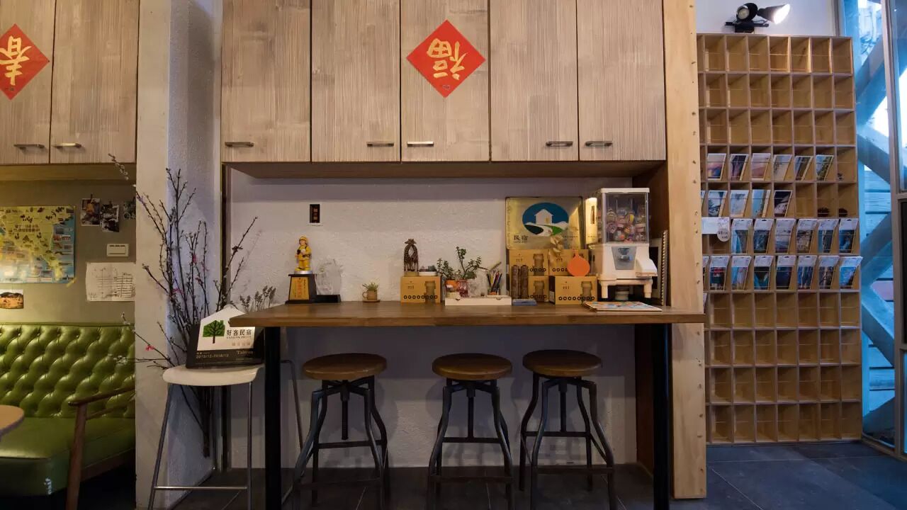 A bar area with wooden cabinets, a green cushioned seating area, and a display of books and magazines.