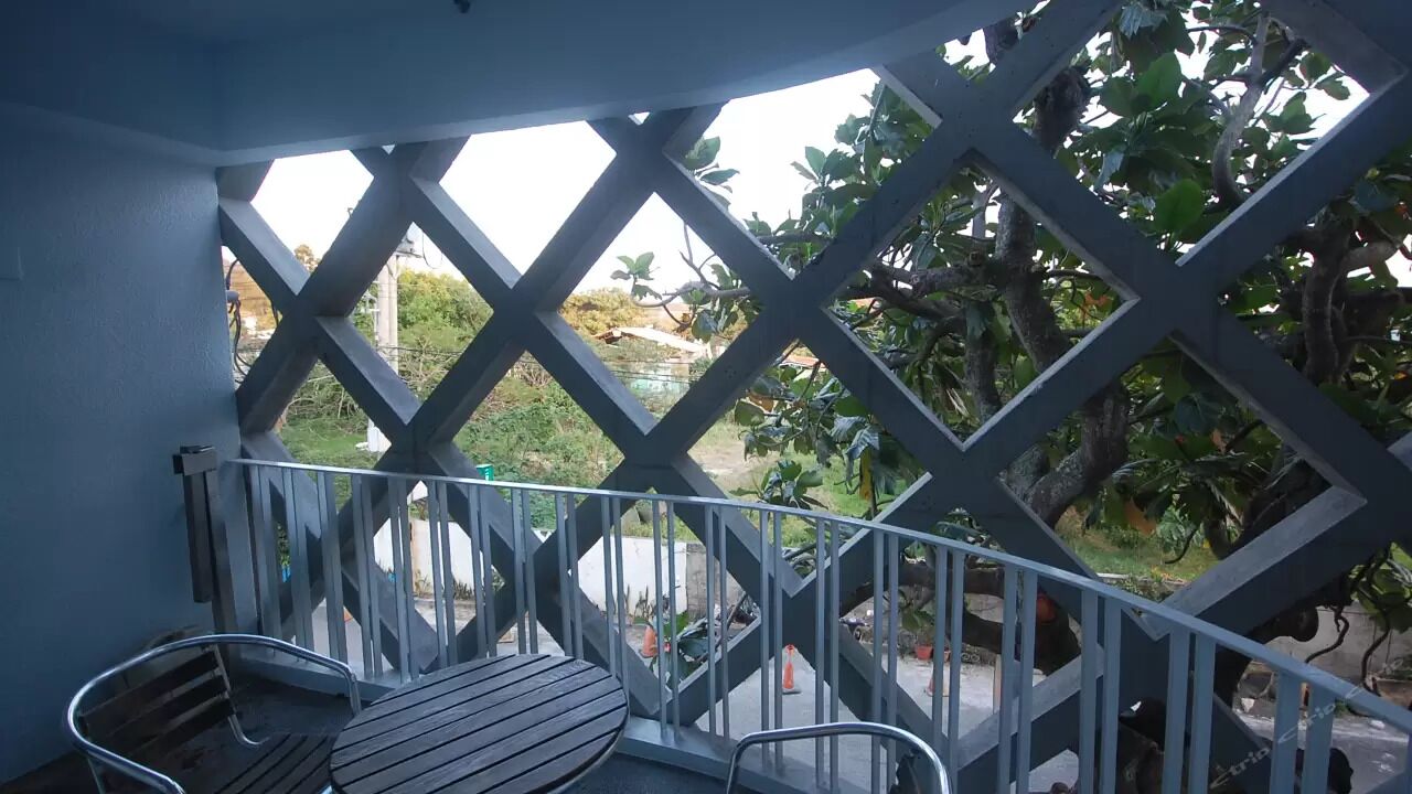 Un balcón con mesa de madera y sillas metálicas, con vista a un jardín con árboles y un sendero.