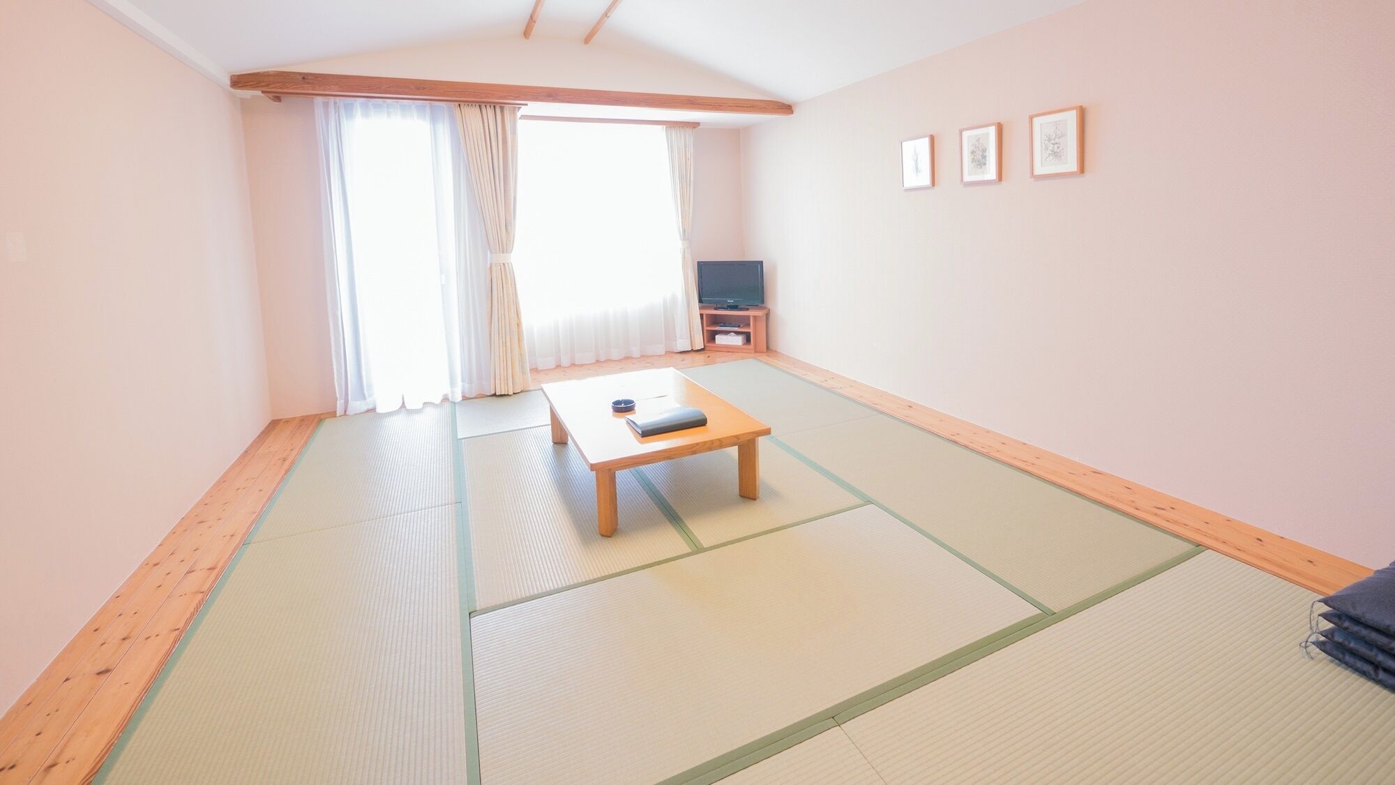 Een kamer met tatami vloerbedekking, een lage houten tafel, een televisie en een raam met gordijnen.