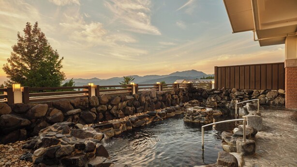 A stone pool with a wooden deck, surrounded by a stone wall and a wooden fence, with a mountain view in the background.