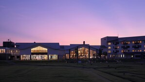 A modern building complex with large windows and a flat roof, surrounded by a grassy field.
