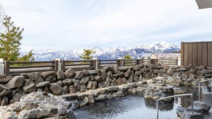 A stone hot spring with a wooden fence and a view of snow-capped mountains in the background.