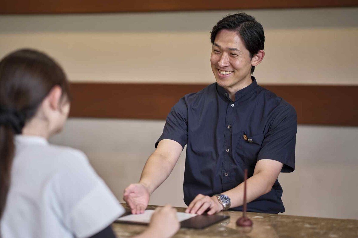 A person seated at a reception desk, interacting with a staff member behind the counter.
