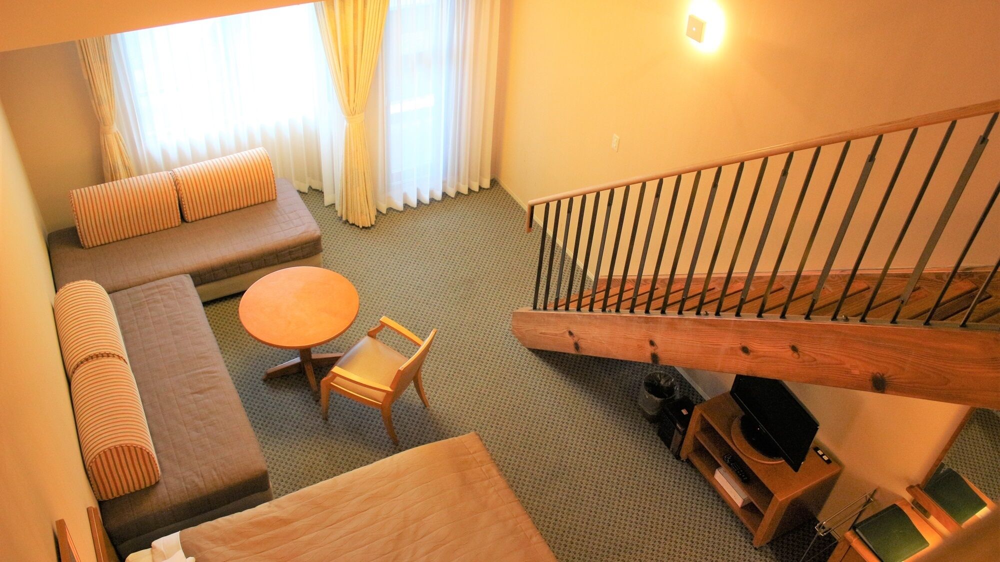 Een hotelkamer met een bank, een ronde tafel, een stoel, een trap en een tv-meubel.