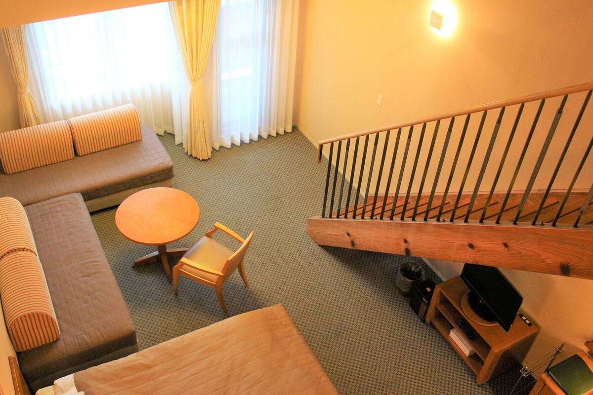 Ein Hotelzimmer mit einer Couch, einem runden Tisch, einem Sessel, einer Treppe und einem Fernsehschrank.
