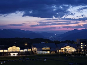 Un hotel con varias construcciones, amplias ventanas y vistas a montañas al fondo.