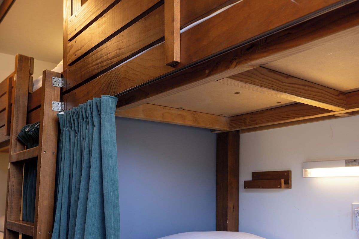 Una cama litera con cortina, vigas de madera y colchón blanco.