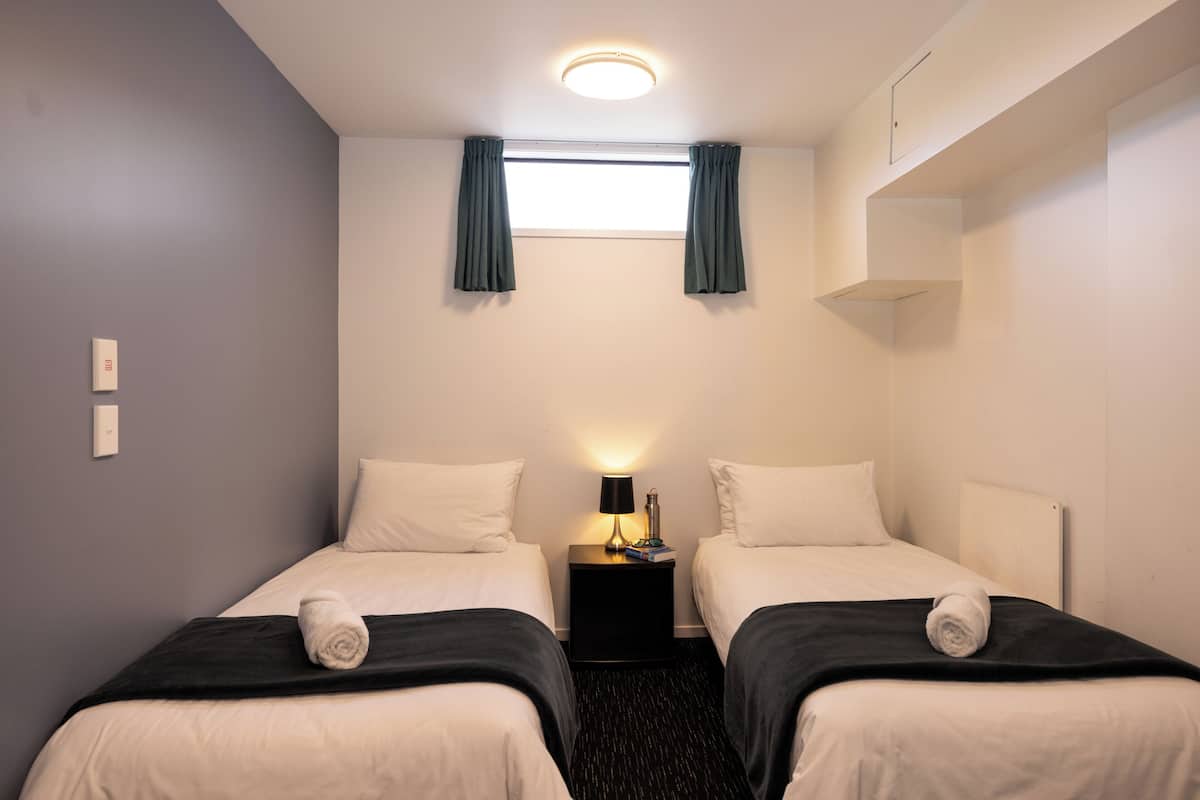 Una habitación de hotel con dos camas, una mesita de noche con lámpara y una ventana con cortinas.