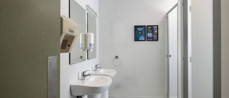 A bathroom with two sinks, a hand dryer, and a mirror. There are two informational posters on the wall.