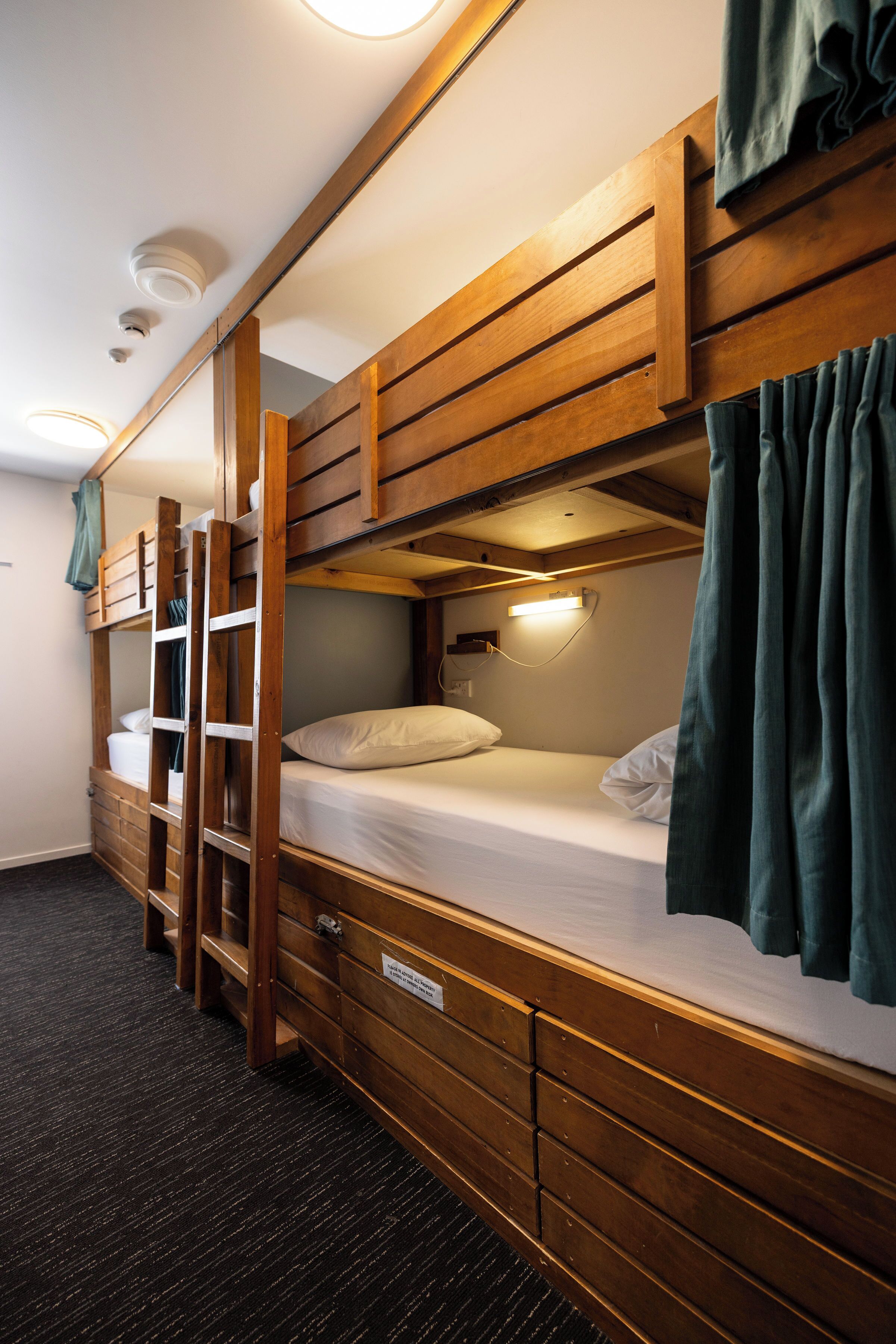 Une chambre avec un lit superposé, une échelle en bois, une table de chevet et une lampe fixée au mur.
