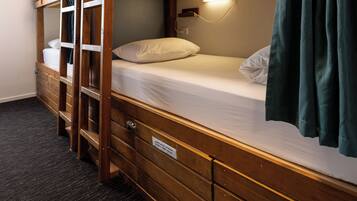 Une chambre avec un lit superposé, une échelle en bois, une table de chevet et une lampe fixée au mur.