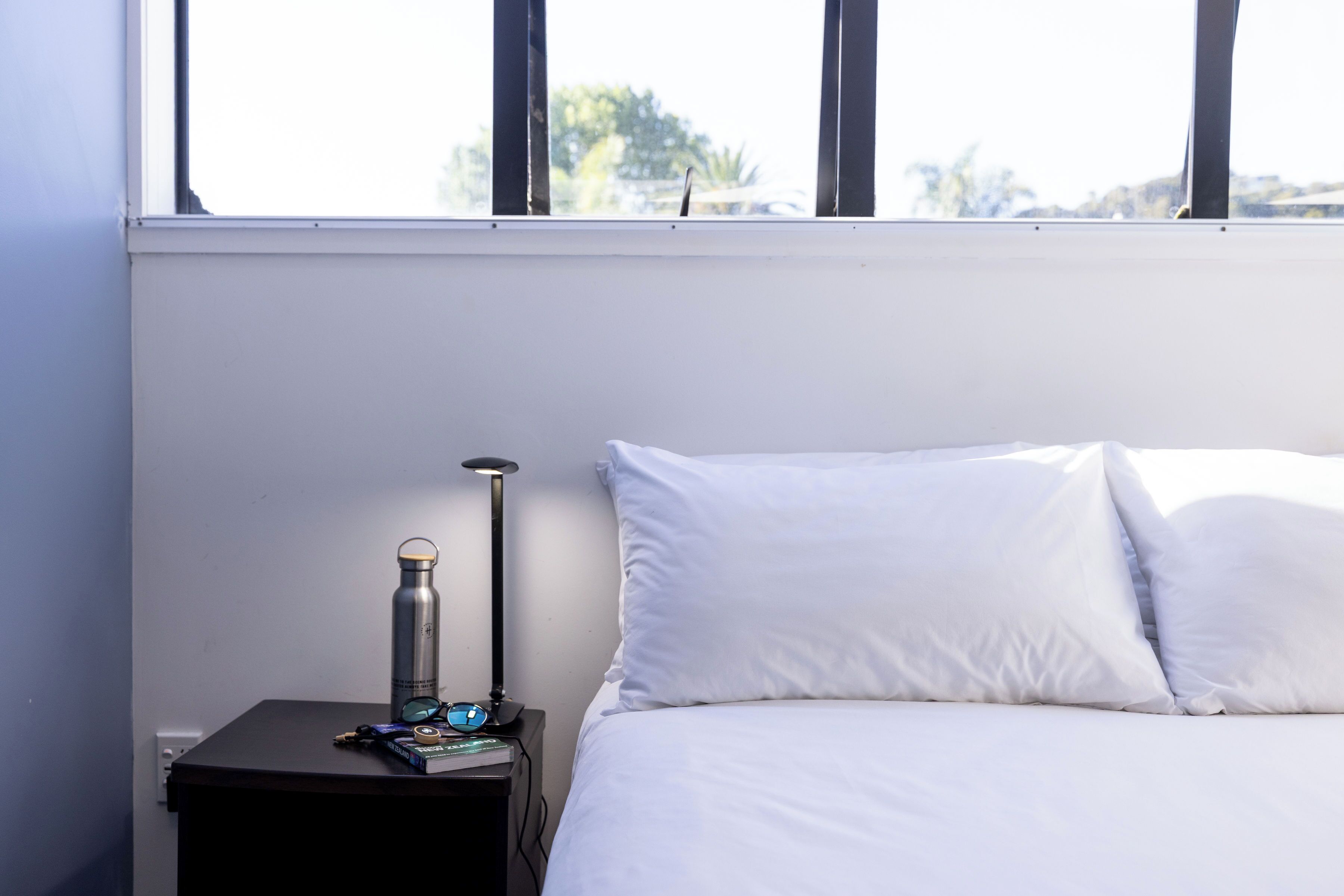 A neatly made bed with white linens, a small bedside table with a lamp, a water bottle, and a book.