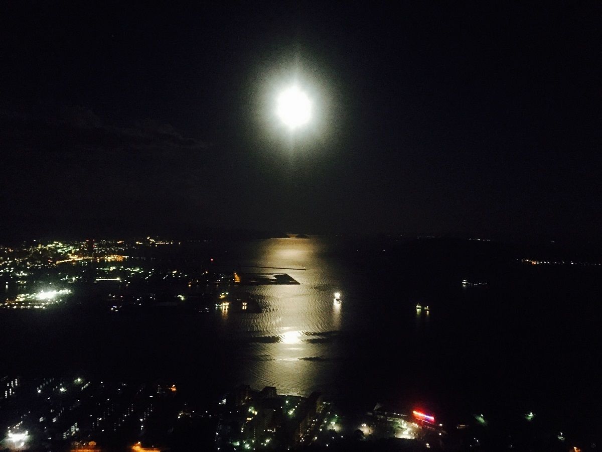 Una vista notturna di una città costiera con una luna piena che si riflette sull'acqua.