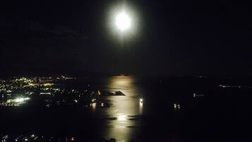 Una vista notturna di una città costiera con una luna piena che si riflette sull'acqua.