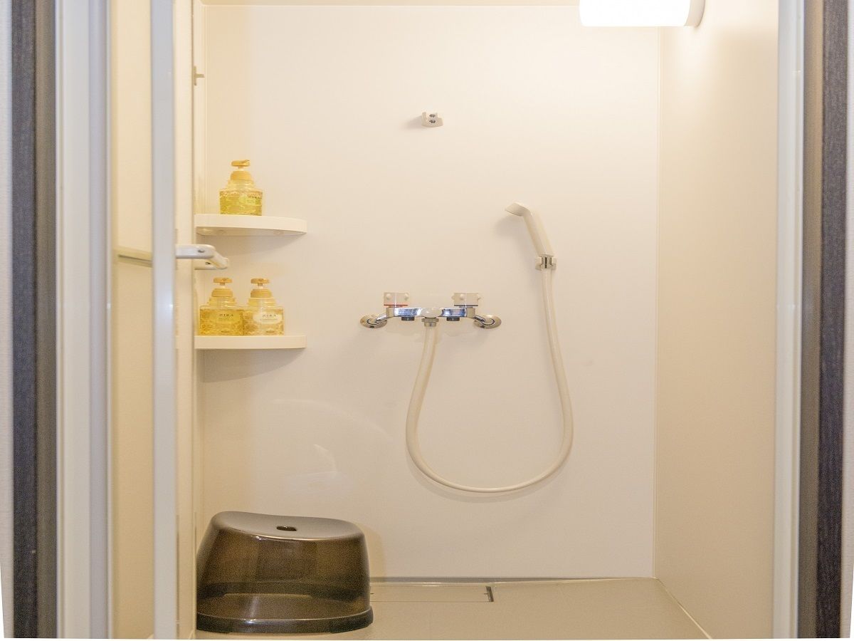 A small, enclosed shower area with a handheld showerhead, a soap dispenser, and a small stool.