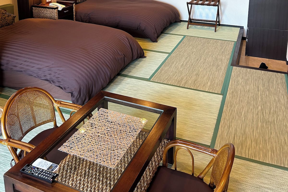 Camera d'albergo con due letti, un tavolino, una sedia, una lampada e una TV a muro.