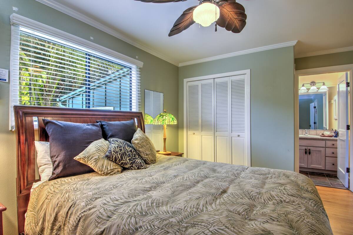 A bedroom with a bed, a ceiling fan, and a view of the bathroom.