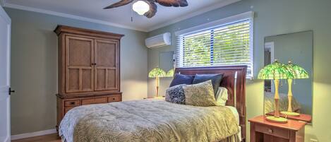 A bedroom with a bed, a ceiling fan, a window with blinds, a nightstand, and a wardrobe.