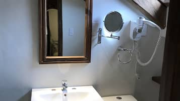 A bathroom with a white sink, a toilet, a mirror, and a hairdryer mounted on the wall.