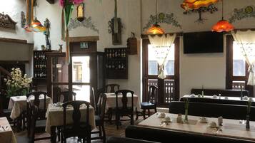 Een restaurantinterieur met houten tafels en stoelen, hangende decoratieve lampen en een wijnrek.