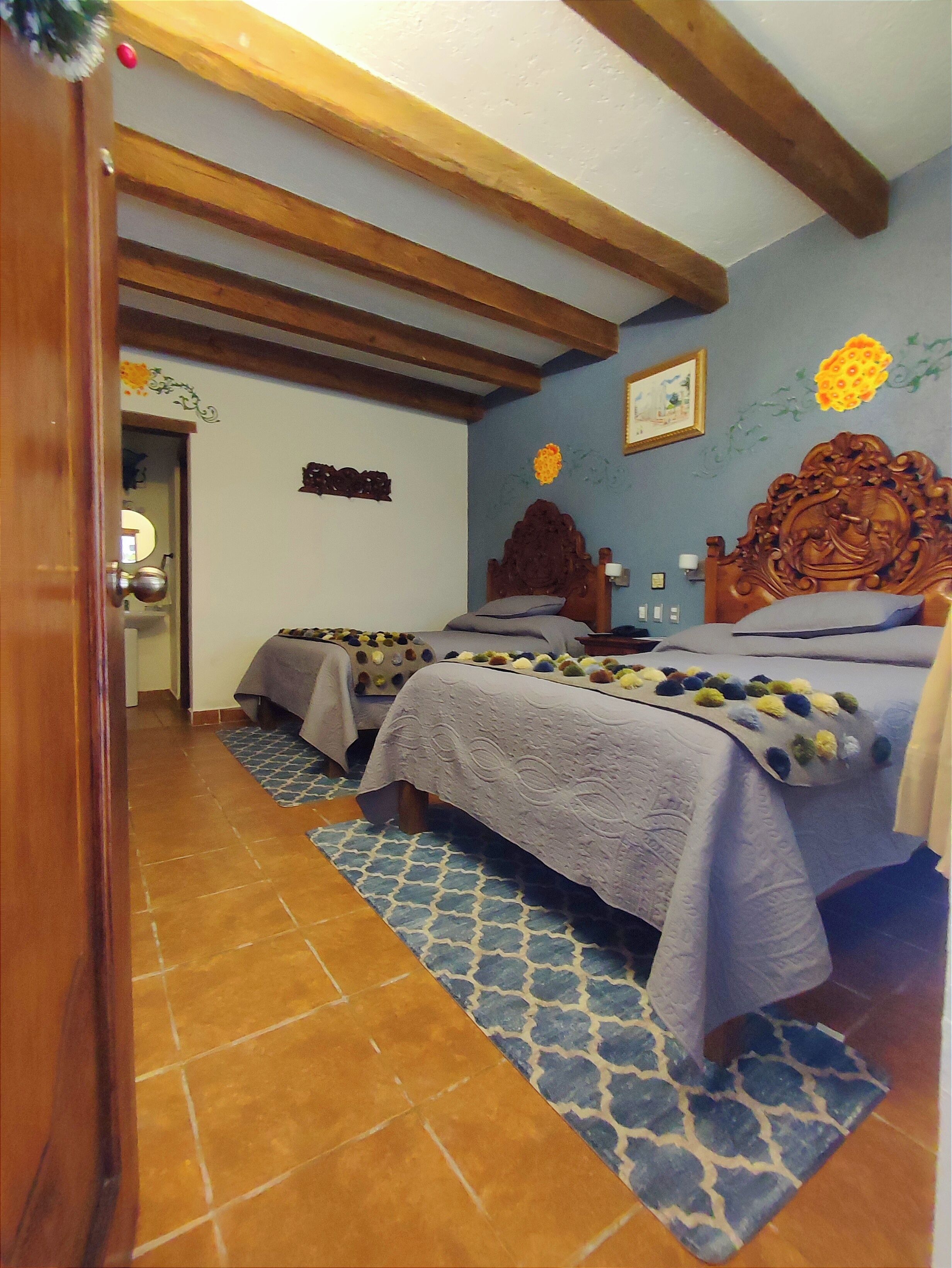 Ein Schlafzimmer mit zwei Betten, Holzbalken, einem gemusterten Teppich und einer Wand mit floralem Dekor.