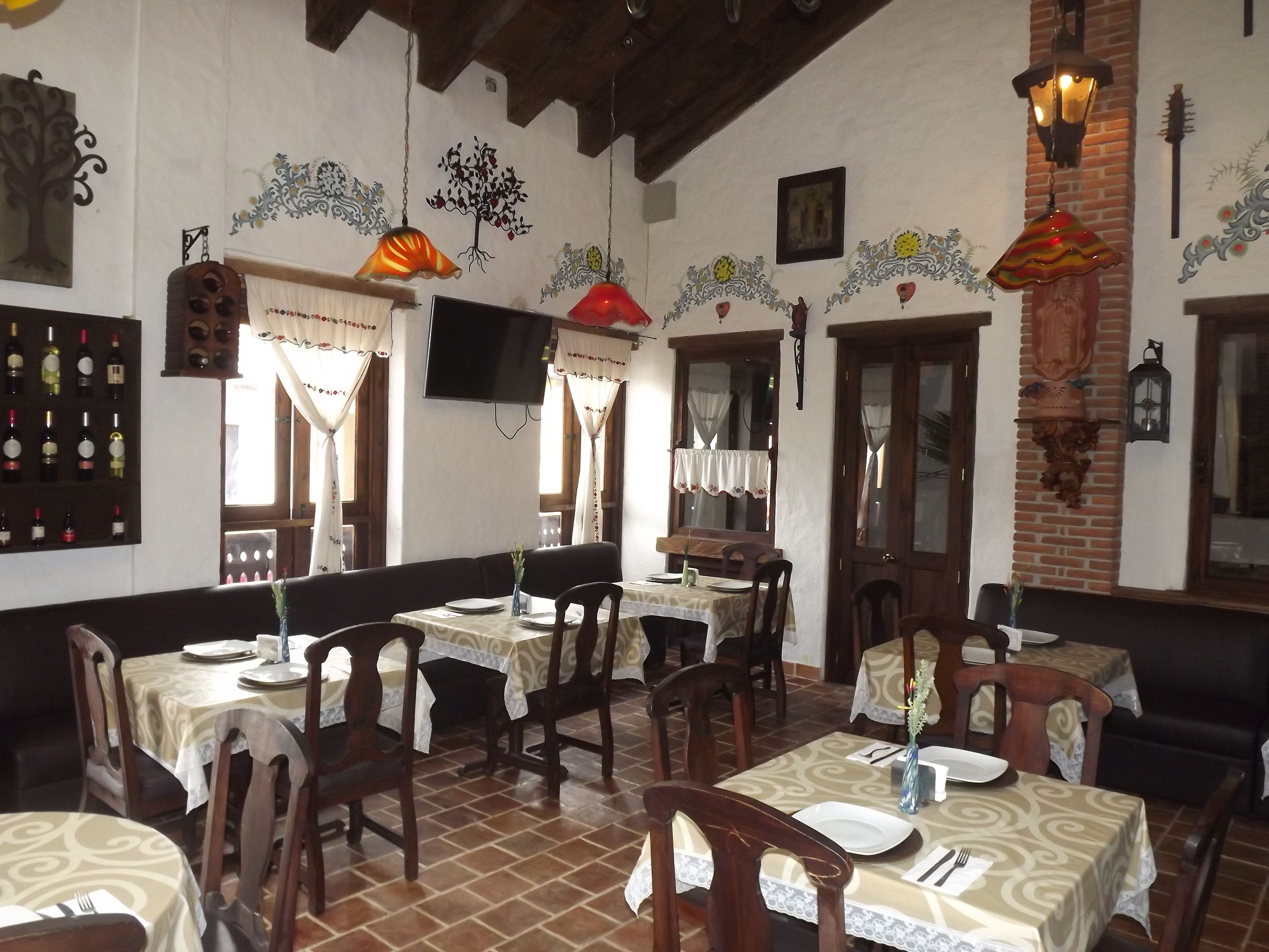 A restaurant with multiple tables and chairs, a TV mounted on the wall, and decorative wall art.