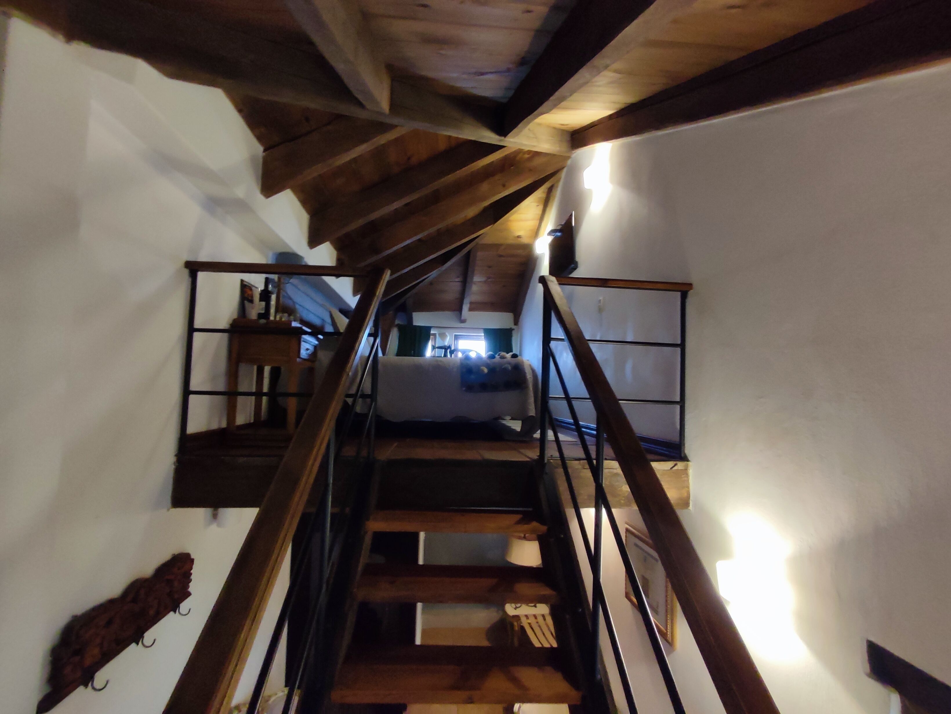 Un escalier en bois avec une rampe métallique menant à une chambre à coucher équipée d’un lit et d’une table de chevet.