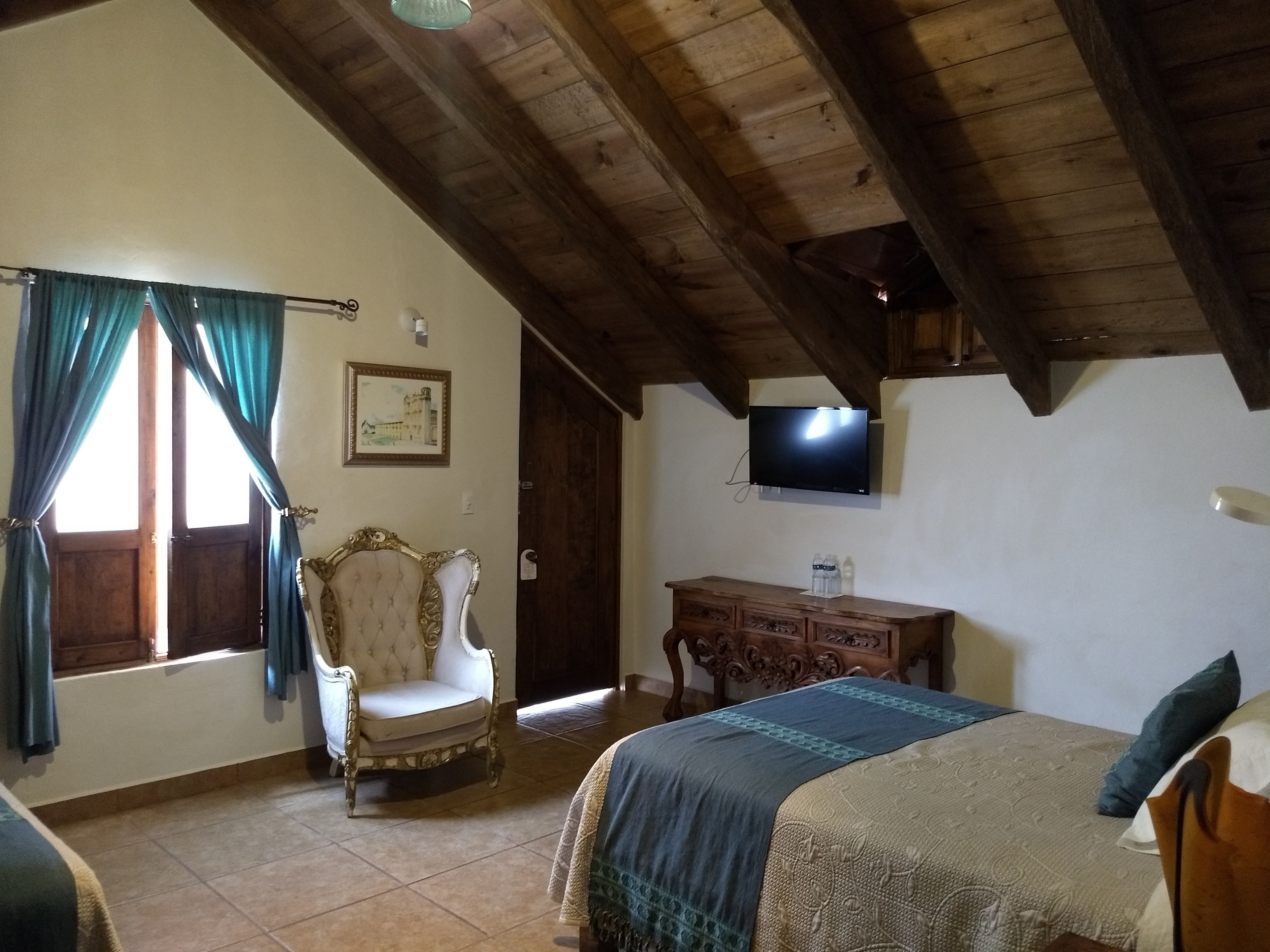 A bedroom with a bed, a chair, a desk, a television, and a window with curtains.