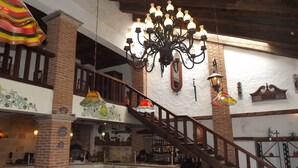 A restaurant with a brick interior, wooden staircase, and hanging chandeliers.