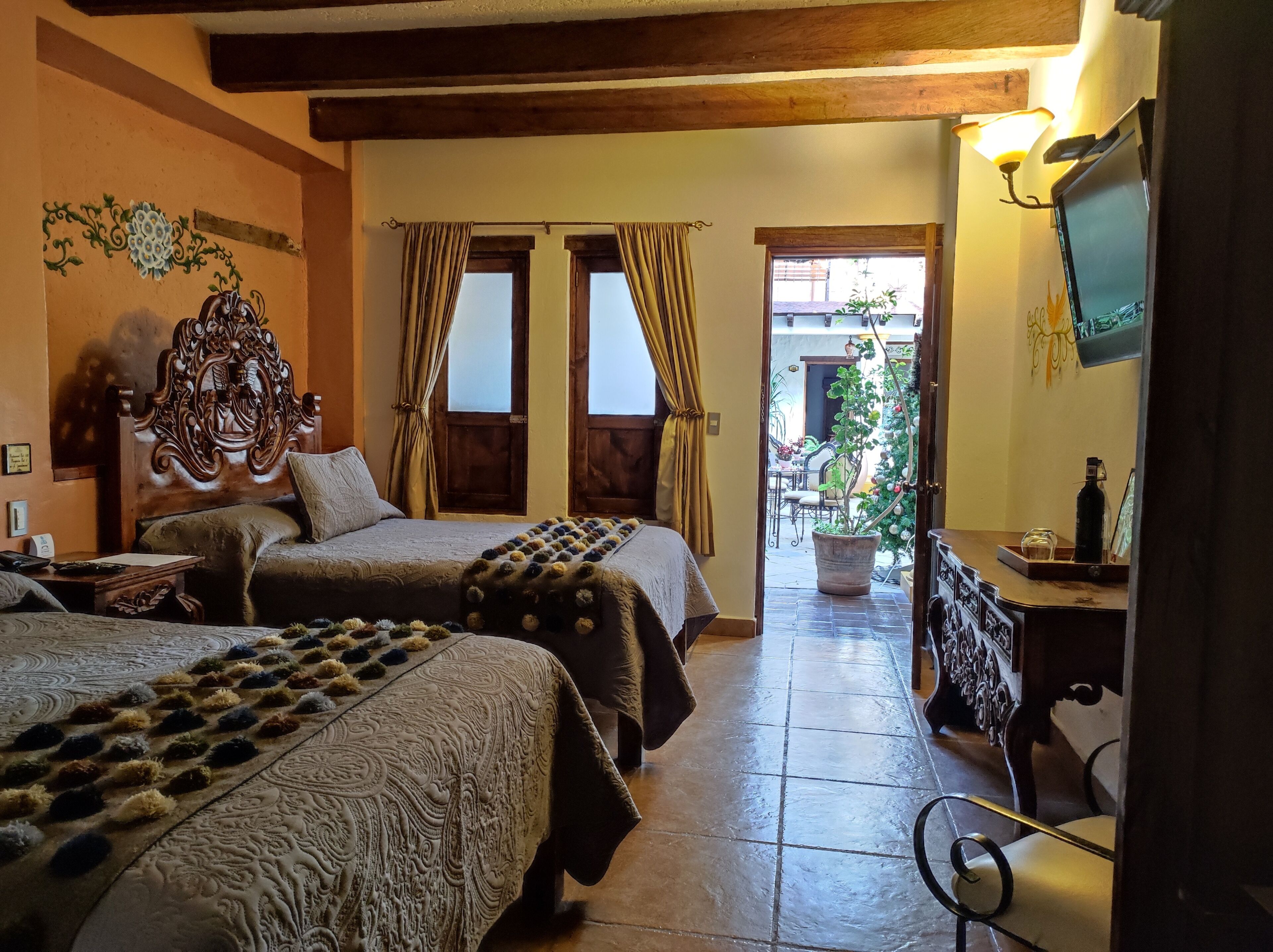 A hotel room with two beds, a wooden headboard, a large potted plant, and a TV on the wall.