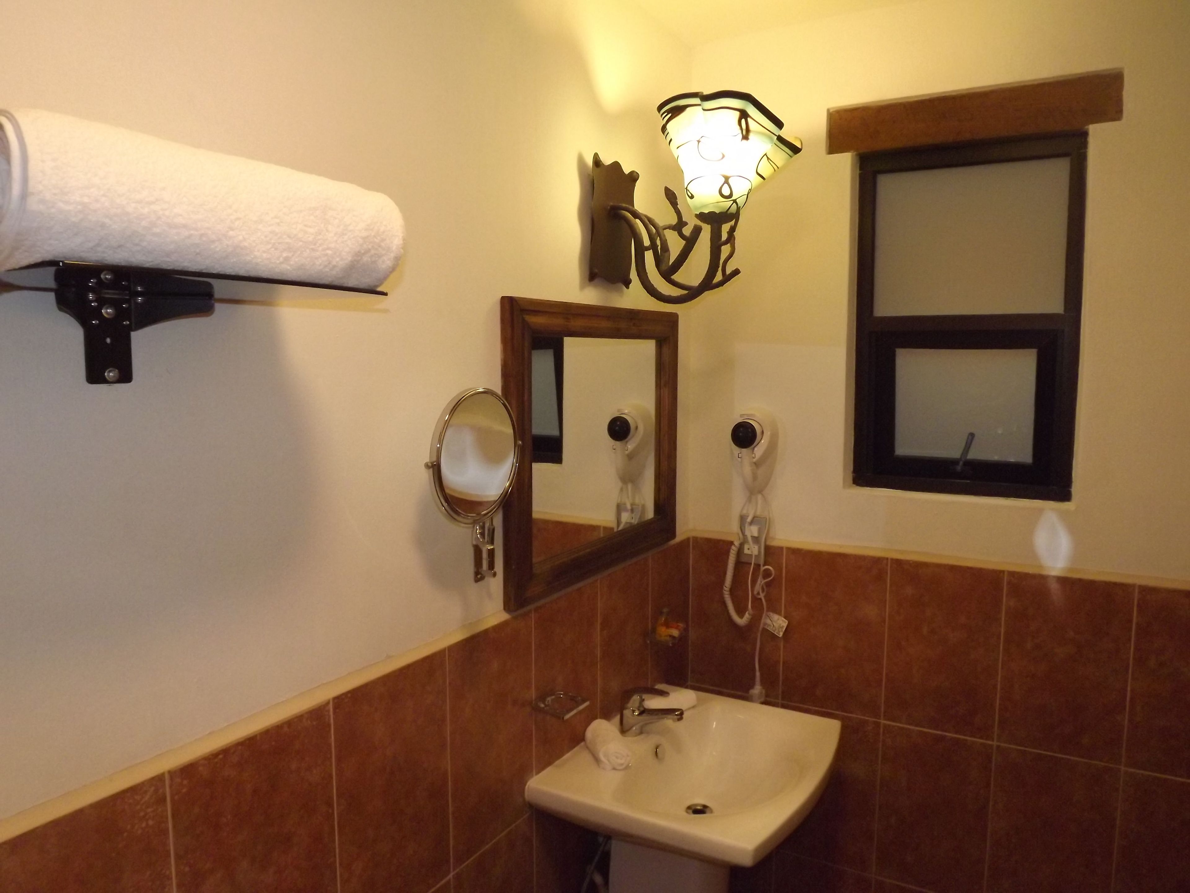 A bathroom with a sink, a mirror, a towel dispenser, and a wall-mounted light fixture.
