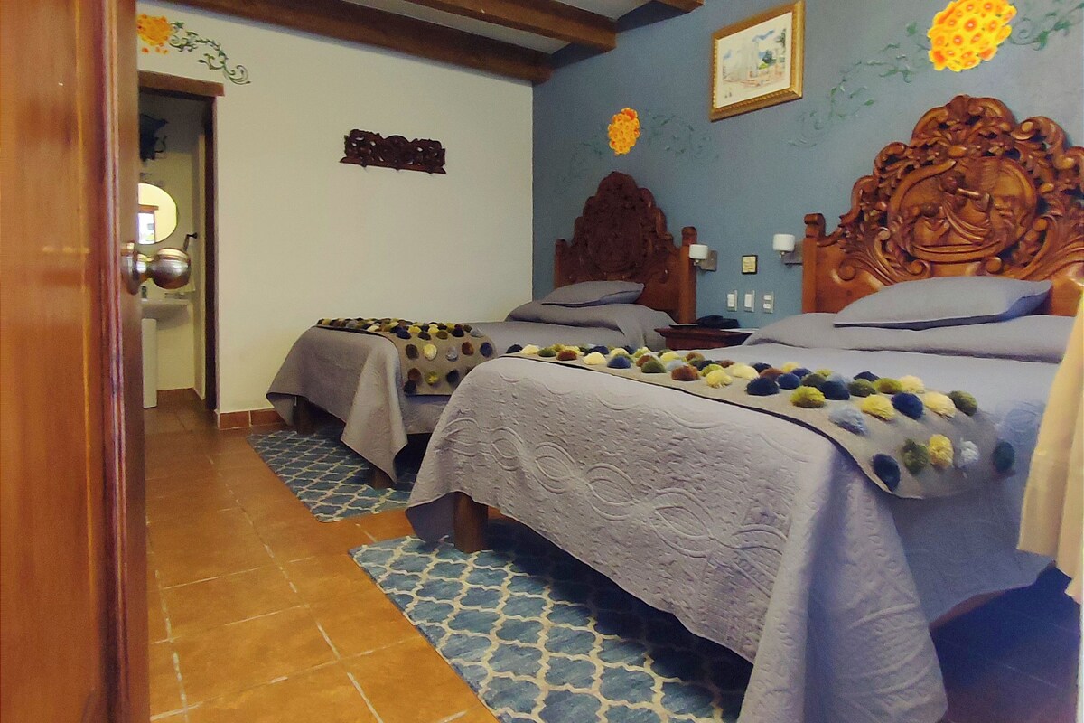 Une chambre avec deux lits, des poutres en bois, un tapis à motifs et un mur orné d’un motif floral.
