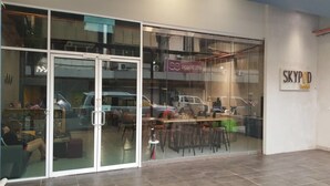 A hotel interior with a reception desk, seating area, and a visible car in the background. - SKYPOD Hostel (Kota Kinabalu)