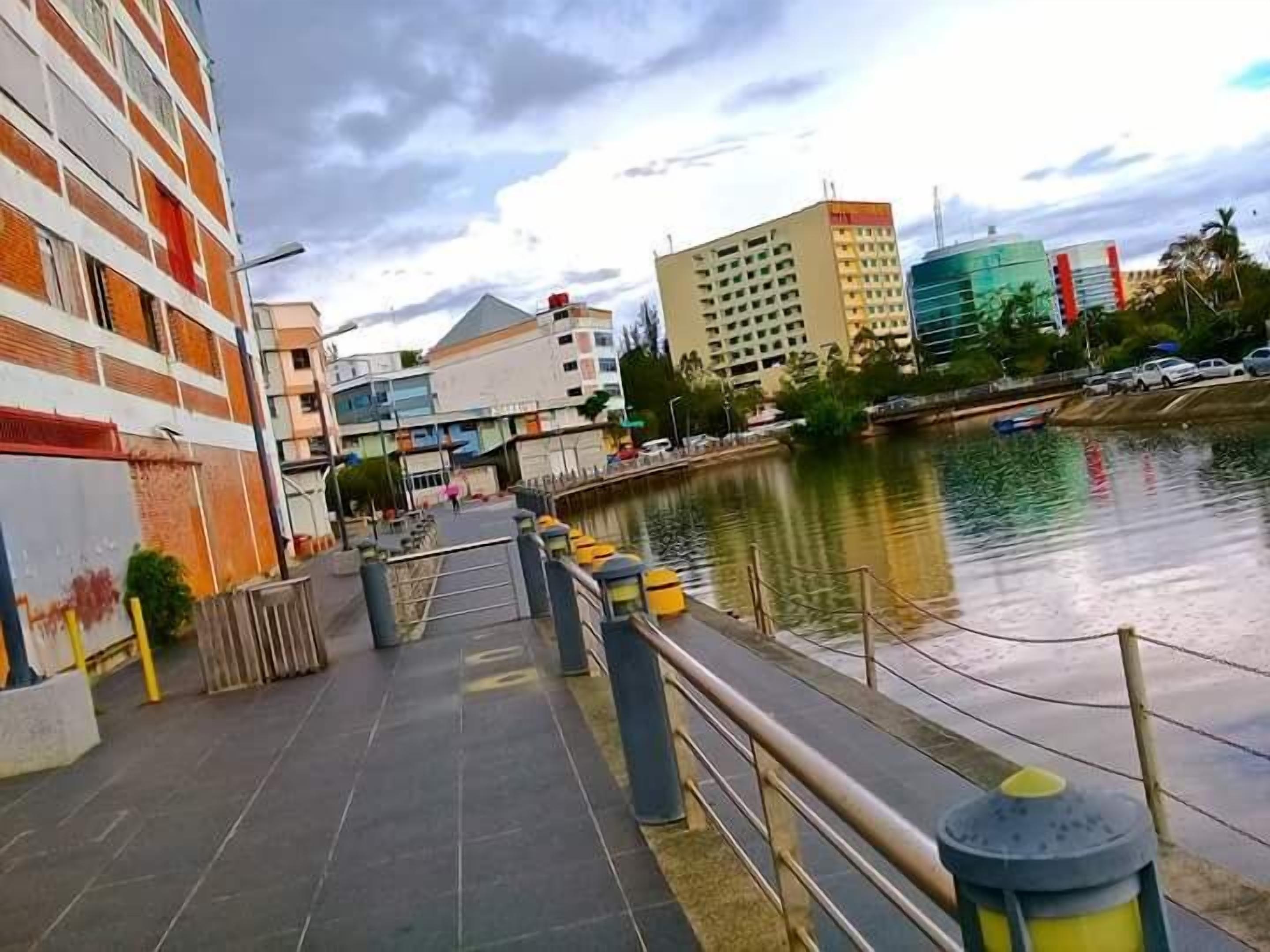 A riverside walkway with modern buildings, a pedestrian bridge, and a calm water body. - SKYPOD Hostel (Kota Kinabalu)