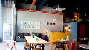 A modern interior with a long wooden table, multiple chairs, a sofa, and a yellow counter with magazines. - SKYPOD Hostel (Kota Kinabalu)