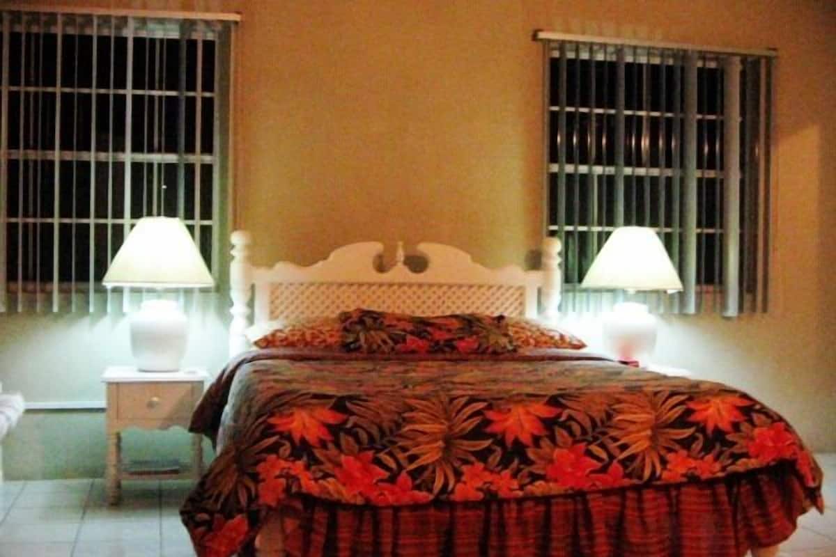A bedroom with a bed, two bedside lamps, a nightstand, and barred windows.