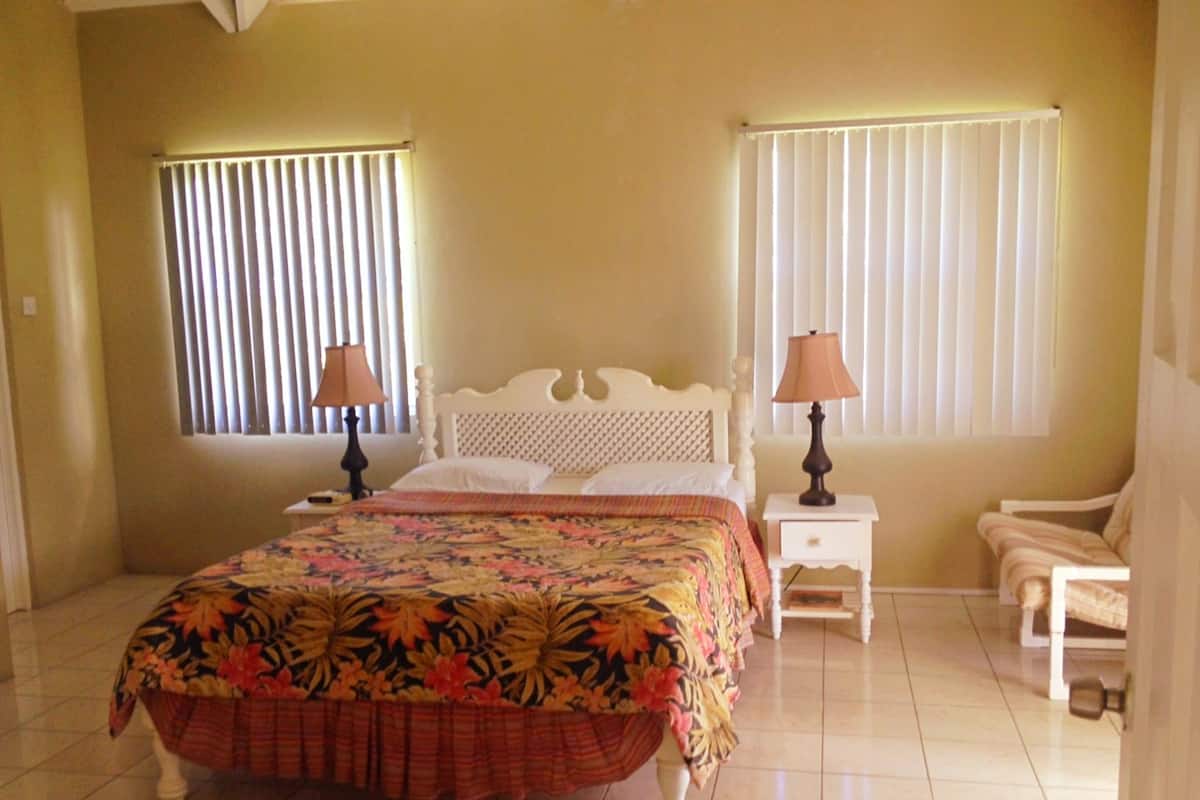 A bedroom with a bed, two bedside tables with lamps, a chair, and a window with blinds.