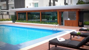 Un espace piscine moderne avec une terrasse en bois, des chaises longues et un comptoir d’accueil.