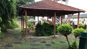 A gazebo with a tiled roof, surrounded by a garden with various plants and a stone pathway. - International House (George Town)