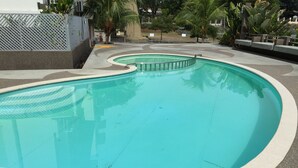 A swimming pool with a curved design, surrounded by a concrete deck and palm trees. - International House (George Town)