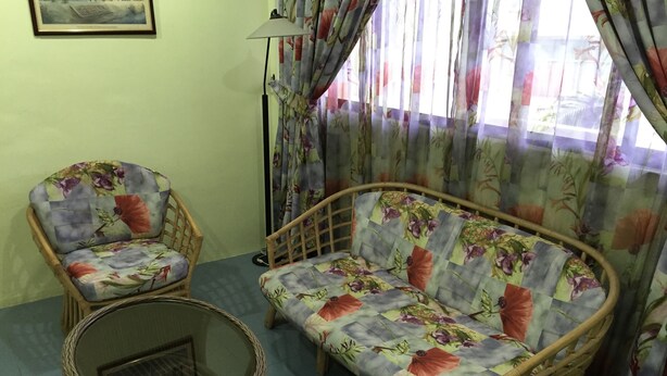 A living room with a sofa and two armchairs, a wicker coffee table, and a floor lamp. - International House (George Town)