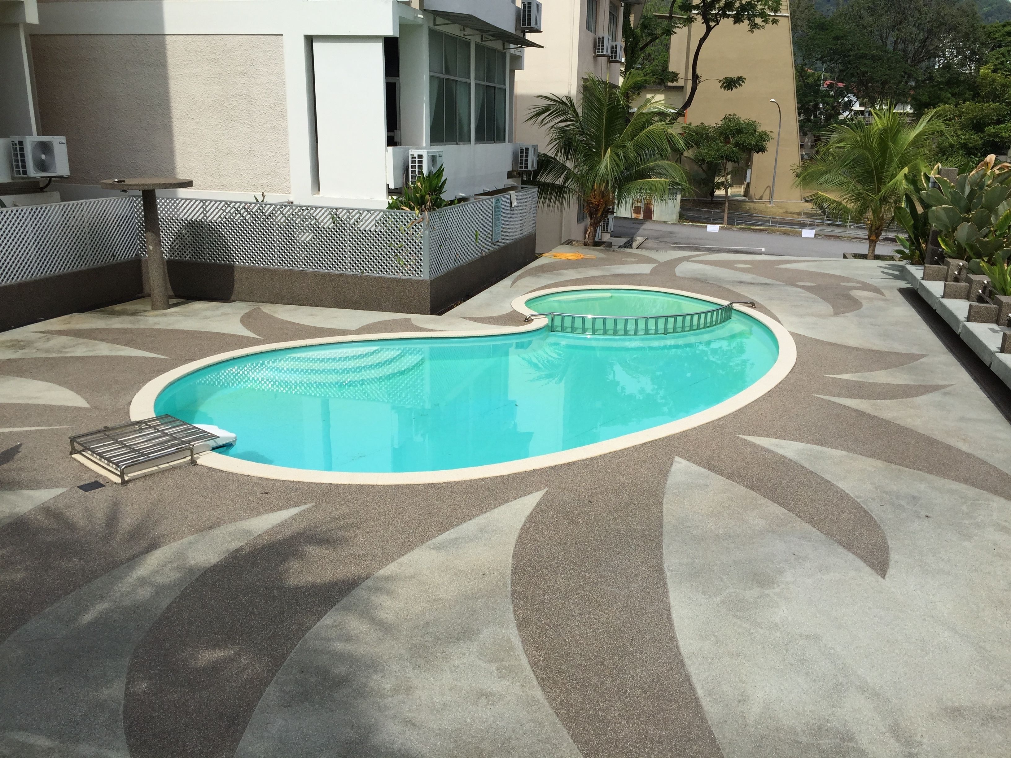 A swimming pool with a wavy design, surrounded by a patterned walkway and palm trees.