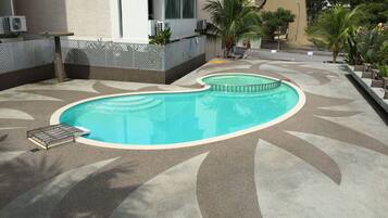 Una piscina con un design ondulato, circondata da un percorso pedonale decorato e da palme.
