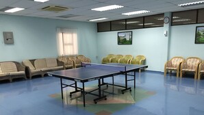A room with a ping pong table, several chairs, a clock, and a window with blinds. - International House (George Town)