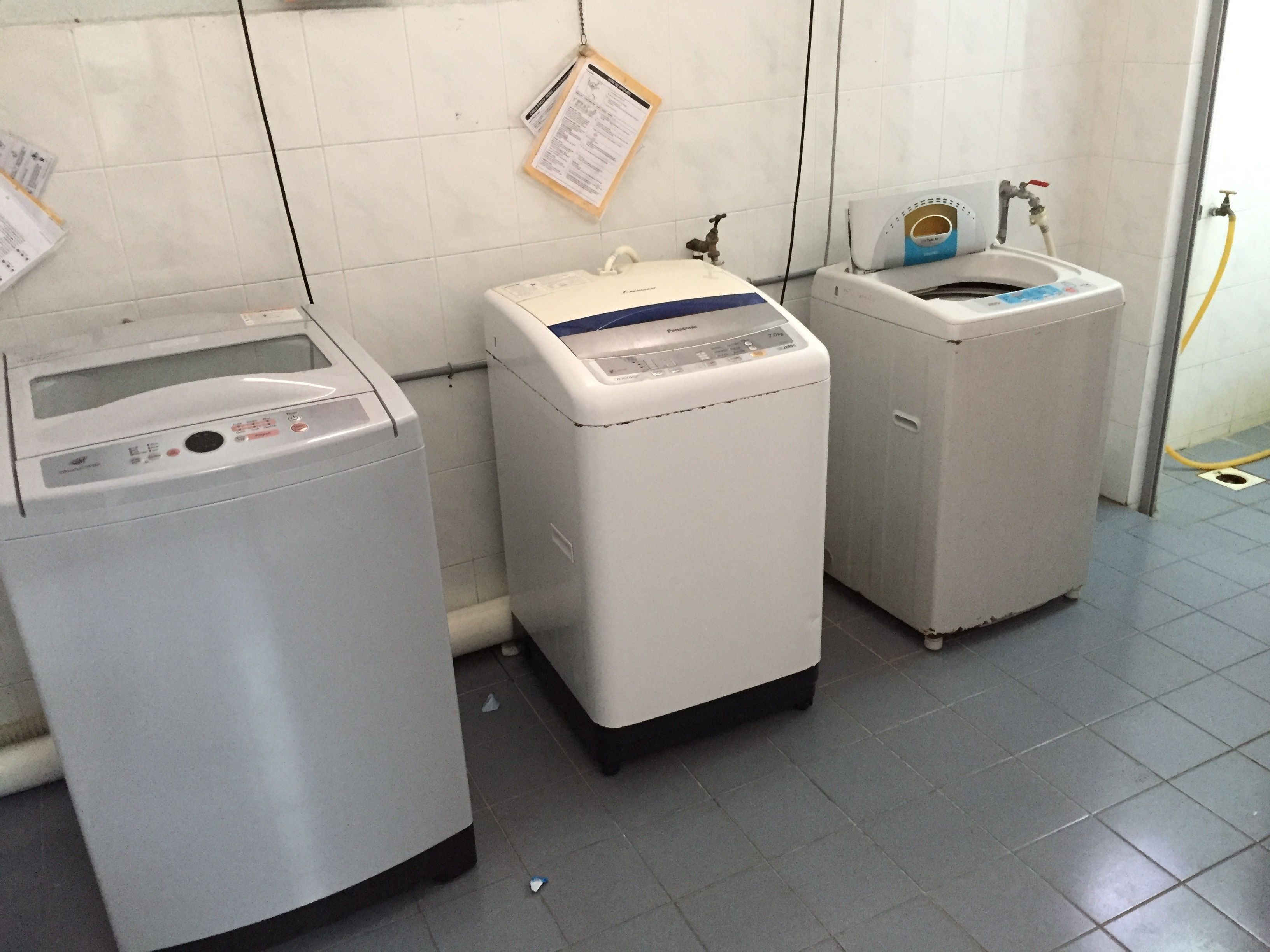 A laundry area with three washing machines, a water heater, and a water meter.