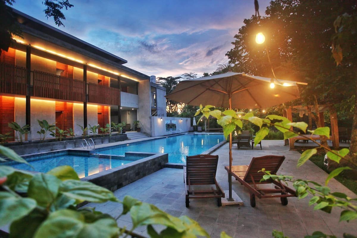 Ein moderner Poolbereich mit Liegestühlen und einer überdachten Lounge, umgeben von einem Gebäude mit warmer Beleuchtung.