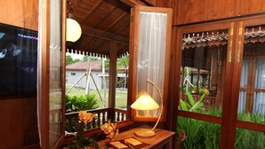 A wooden room with a wooden desk, a lamp, a potted plant, and a television. - Amata Borobudur Resort (Mungkid)
