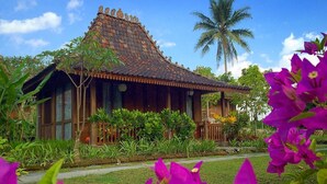 A traditional wooden house with a tiled roof, surrounded by lush greenery and vibrant flowers. - Amata Borobudur Resort (Mungkid)