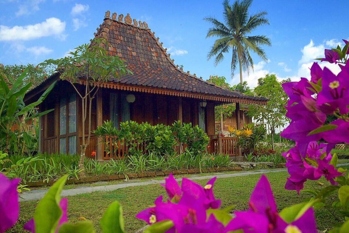 Ein traditionelles Holzhaus mit Ziegeldach, umgeben von üppigem Grün und leuchtenden Blumen.